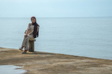 Asyalı Müslüman kadınlar rıhtımda oturur. İskelede, arka planda oturan Asyalı kadınların görünüşü ve balıkların boş alanı için sakin deniz..