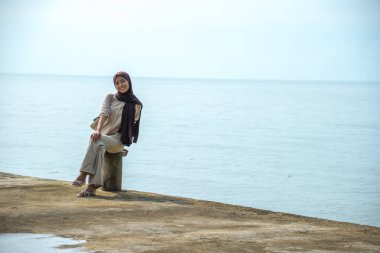 Asyalı Müslüman kadınlar rıhtımda oturur. İskelede, arka planda oturan Asyalı kadınların görünüşü ve balıkların boş alanı için sakin deniz..