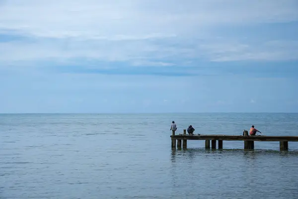 Jepara Merkez Java, 4 Nisan 2025, erkekler rıhtımda balık tutuyor. Balıkçılar sakin deniz suyunda iskelede balık tutuyorlar..