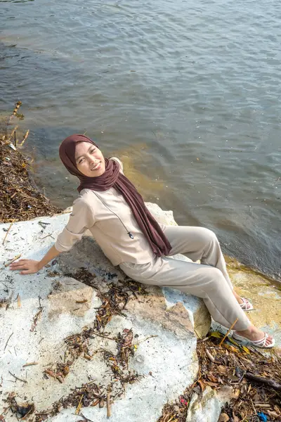 Müslüman Asyalı kadınların deniz taşının üzerinde oturması, Asyalı kadınların boş uzay reklamları için deniz suyunun arka planına sahip bir taşın üzerinde oturmaları..