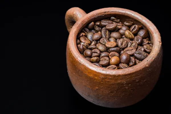 Kahve çekirdekleri ile dolu kil fincanın görüntüsü, siyah arka planda kilden fincanda kavrulmuş kahve çekirdekleri, siyah fincanda kahve çekirdekleri..