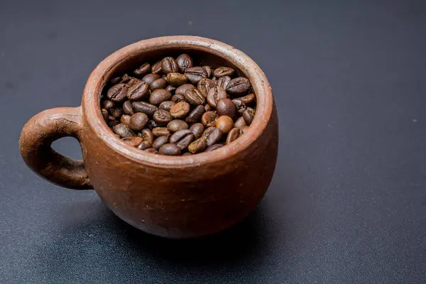 Kahve çekirdekleri ile dolu kil fincanın görüntüsü, siyah arka planda kilden fincanda kavrulmuş kahve çekirdekleri, siyah fincanda kahve çekirdekleri..
