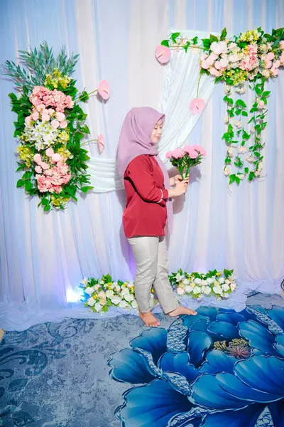 Bir şenlik etkinliğinde elinde sentetik çiçek dekoru olan Asyalı Müslüman kadın poz veriyor..