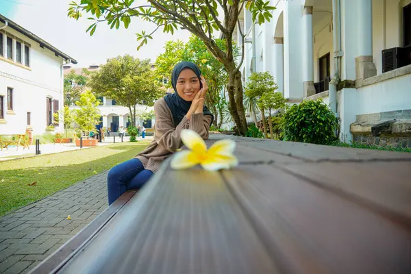 Cava 'lı bir kadın gölgeli bir ağacın altında Kampoja çiçekleriyle bankta oturuyor..