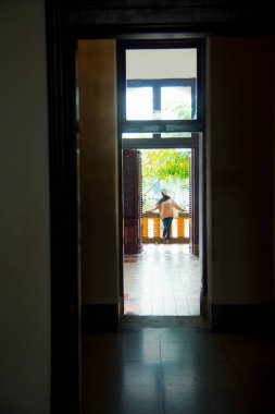 Klasik mimarinin açık kapısının ortasında duran tesettürlü kadın gölgeli ağaçların arka planında parlak doğal ışık ile duvar koridoru inşa ediyor.