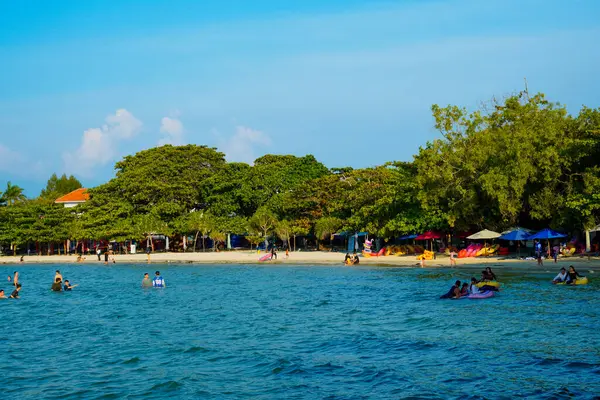 Sahilde ağaçların olduğu sığ bir kumsalda küçük dalgalar kırılıyor ve reklam alanı için açık bir gökyüzü var..