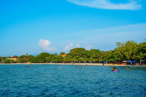 Sahilde ağaçların olduğu sığ bir kumsalda küçük dalgalar kırılıyor ve reklam alanı için açık bir gökyüzü var..