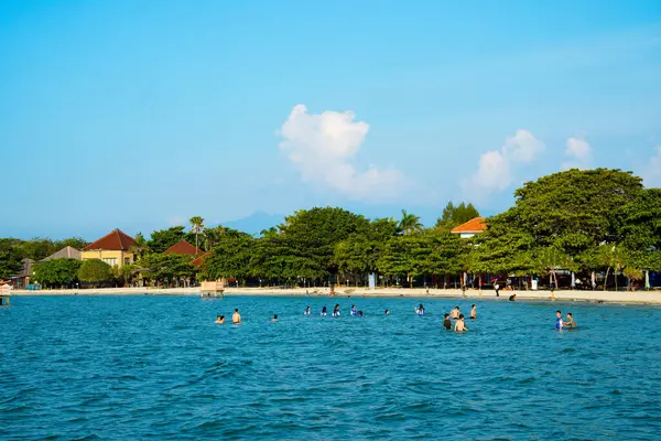 Sahilde ağaçların olduğu sığ bir kumsalda küçük dalgalar kırılıyor ve reklam alanı için açık bir gökyüzü var..