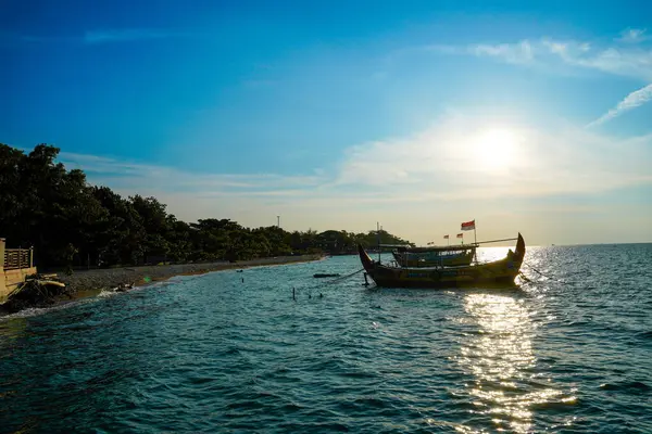 Alacakaranlık güneşinin arka planı ve reklam odası için mavi gökyüzü olan kumlu sahil şeridinin yanındaki balıkçı teknesinin manzarası..