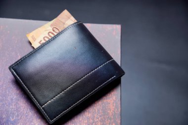 Beyaz dikişli siyah deri cüzdanın temiz görüntüsü reklam alanı için koyu bir zemin üzerinde rupiah banknotları olan siyah cüzdan dışarı fırlamış rupiah banknotlar.