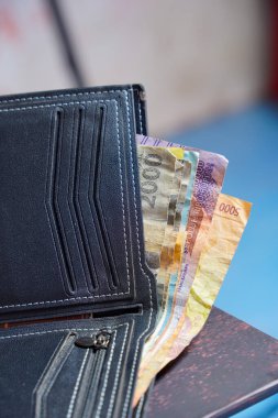 Beyaz dikişli siyah deri cüzdanın temiz görüntüsü reklam alanı için koyu bir zemin üzerinde rupiah banknotları olan siyah cüzdan dışarı fırlamış rupiah banknotlar.