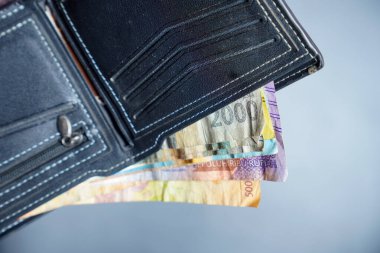 Beyaz dikişli siyah deri cüzdanın temiz görüntüsü reklam alanı için koyu bir zemin üzerinde rupiah banknotları olan siyah cüzdan dışarı fırlamış rupiah banknotlar.