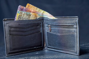 Reklam alanı için siyah arka planda rupiah notlarıyla dolu siyah deriden yapılmış erkek cüzdanı..