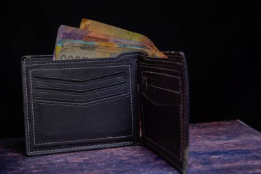 Reklam alanı için siyah arka planda rupiah notlarıyla dolu siyah deriden yapılmış erkek cüzdanı..