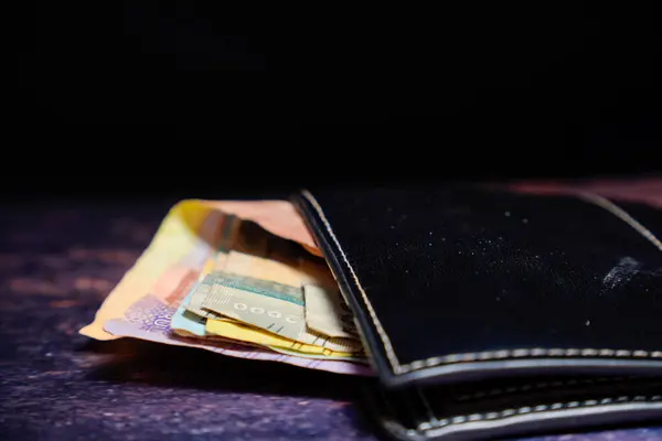 Siyah deri cüzdan. İçinde rupiah banknotları var. Reklam alanı için koyu bir arka planı var..