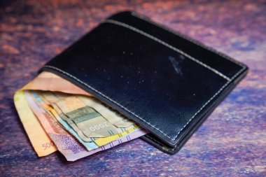 Siyah deri cüzdan. İçinde rupiah banknotları var. Reklam alanı için koyu bir arka planı var..