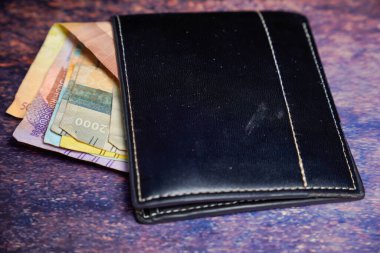 Siyah deri cüzdan. İçinde rupiah banknotları var. Reklam alanı için koyu bir arka planı var..