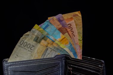 Reklam alanı için siyah arka planda rupiah notlarıyla dolu siyah deriden yapılmış erkek cüzdanı..