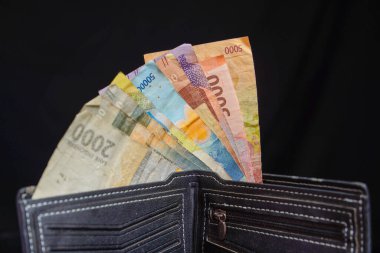 Reklam alanı için siyah arka planda rupiah notlarıyla dolu siyah deriden yapılmış erkek cüzdanı..