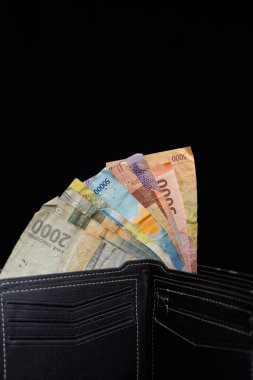 Reklam alanı için siyah arka planda rupiah notlarıyla dolu siyah deriden yapılmış erkek cüzdanı..
