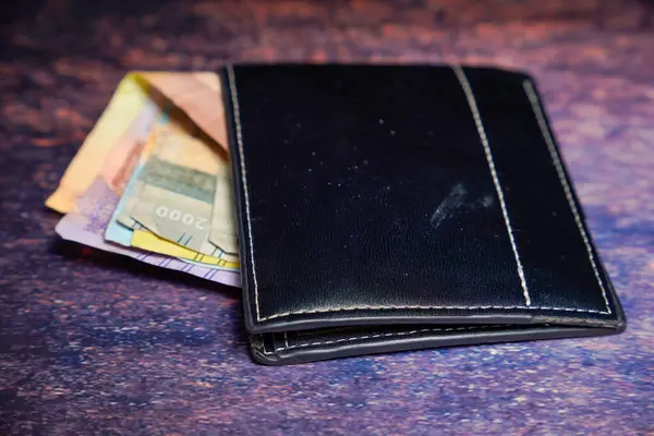Siyah deri cüzdan. İçinde rupiah banknotları var. Reklam alanı için koyu bir arka planı var..