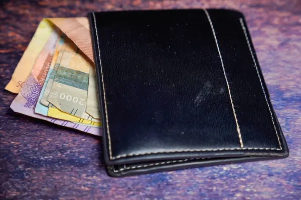 Siyah deri cüzdan. İçinde rupiah banknotları var. Reklam alanı için koyu bir arka planı var..