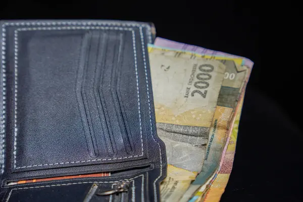 Siyah deri cüzdan. İçinde rupiah banknotları olan beyaz dikişler. Reklam alanı için koyu bir arka plan..