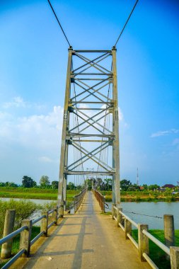 Reklam alanı için açık bir gökyüzü zeminine karşı demirden bir iskeleti olan yüksek bir asma köprü kulesi. Çelik bir asma köprü, parlak mavi gökyüzünün altında yeşilliklerle çevrili bir nehir boyunca uzanır..