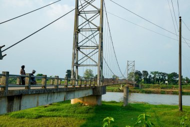 Nehir üzerindeki uzun asma köprü. Etrafı tarlalarla çevrili. Reklam alanı için temiz bir gökyüzü arkaplanı var..