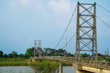 Nehir üzerindeki uzun asma köprü. Etrafı tarlalarla çevrili. Reklam alanı için temiz bir gökyüzü arkaplanı var..