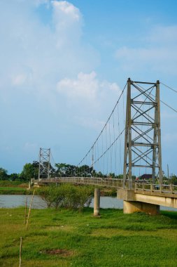 Nehir üzerindeki uzun asma köprü. Etrafı tarlalarla çevrili. Reklam alanı için temiz bir gökyüzü arkaplanı var..