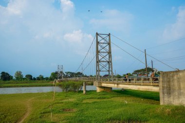 Nehir üzerindeki uzun asma köprü. Etrafı tarlalarla çevrili. Reklam alanı için temiz bir gökyüzü arkaplanı var..