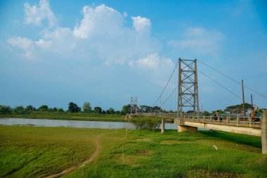 Nehir üzerindeki uzun asma köprü. Etrafı tarlalarla çevrili. Reklam alanı için temiz bir gökyüzü arkaplanı var..