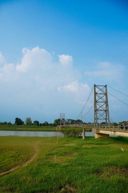 Nehir üzerindeki uzun asma köprü. Etrafı tarlalarla çevrili. Reklam alanı için temiz bir gökyüzü arkaplanı var..