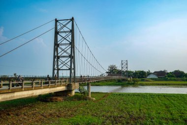 Nehir üzerindeki uzun asma köprü. Etrafı tarlalarla çevrili. Reklam alanı için temiz bir gökyüzü arkaplanı var..