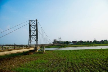 Nehir üzerindeki uzun asma köprü. Etrafı tarlalarla çevrili. Reklam alanı için temiz bir gökyüzü arkaplanı var..