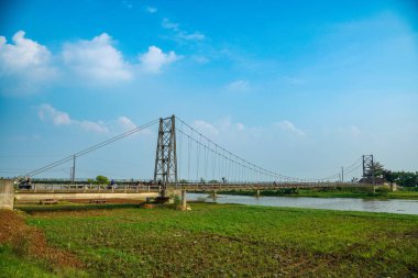 Nehir üzerindeki uzun asma köprü. Etrafı tarlalarla çevrili. Reklam alanı için temiz bir gökyüzü arkaplanı var..