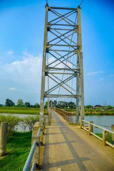 Reklam alanı için açık bir gökyüzü zeminine karşı demirden bir iskeleti olan yüksek bir asma köprü kulesi. Çelik bir asma köprü, parlak mavi gökyüzünün altında yeşilliklerle çevrili bir nehir boyunca uzanır..