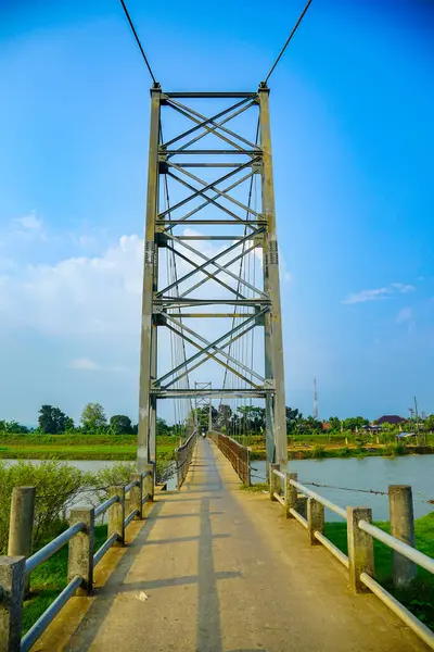 Reklam alanı için açık bir gökyüzü zeminine karşı demirden bir iskeleti olan yüksek bir asma köprü kulesi. Çelik bir asma köprü, parlak mavi gökyüzünün altında yeşilliklerle çevrili bir nehir boyunca uzanır..