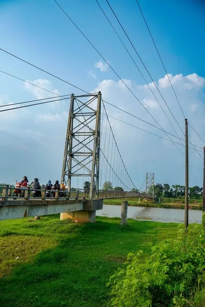 Jepara Central Java, 3 Haziran 2025, bir motosikletçi, reklam alanı için arka planda açık gökyüzü olan bir nehir üzerinden demir asma köprüsünü geçiyor..