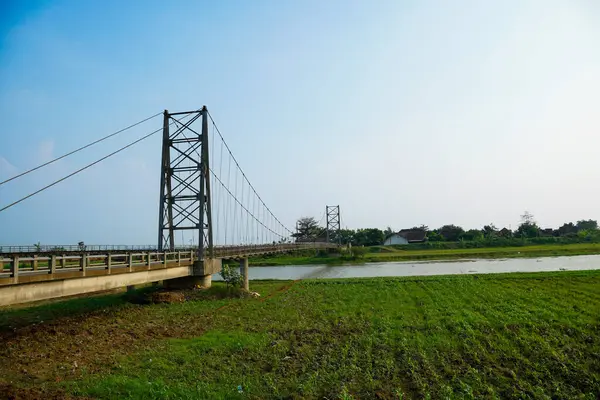 Nehir üzerindeki uzun asma köprü. Etrafı tarlalarla çevrili. Reklam alanı için temiz bir gökyüzü arkaplanı var..