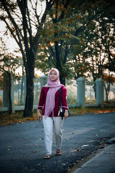 Pembe başörtüsü takan ve parkta yürüyen Asyalı kadın, gündelik giysiler içindeki güzel Müslüman kadın portresi, sonbaharda parkta yürüyen genç Müslüman kadın, yürüyen ve loo