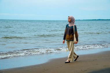 Kumsalda yürüyen tesettürlü Cava 'lı kadınlar, sahilde yürüyen Asyalı Müslüman kadınlar reklam alanı için küçük dalgalar ve boş gökyüzü ile çarpışıyorlar..