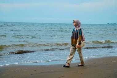 Kumsalda yürüyen tesettürlü Cava 'lı kadınlar, sahilde yürüyen Asyalı Müslüman kadınlar reklam alanı için küçük dalgalar ve boş gökyüzü ile çarpışıyorlar..