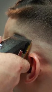 Kolunda dövme olan bir berber berber dükkanında esmer bir adamın saçını kesiyor, kırpma makinesiyle saçını kesiyor. Yüksek kaliteli görüntüler