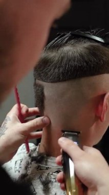 Kolunda dövme olan bir berber berber dükkanında esmer bir adamın saçını kesiyor, kırpma makinesiyle saçını kesiyor. Yüksek kaliteli görüntüler