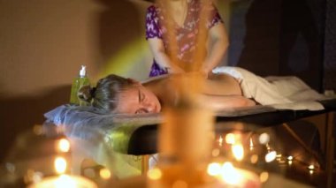 Kozmetik salonundaki usta bir masör genç ve güzel bir kıza masaj yapar. Yakın çekim eller deriyi ve bedeni yağla değiştirir. Mumlarla kaplı karanlık bir ofis.
