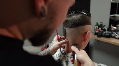 Kolunda dövme olan bir berber berber dükkanında esmer bir adamın saçını kesiyor, kırpma makinesiyle saçını kesiyor. Yüksek kaliteli görüntüler