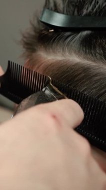 Kolunda dövme olan bir berber berber dükkanında esmer bir adamın saçını kesiyor, kırpma makinesiyle saçını kesiyor. Yüksek kaliteli görüntüler