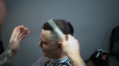 Kolunda dövme olan bir berber berber dükkanında esmer bir adamın saçını kesiyor, kırpma makinesiyle saçını kesiyor. Yüksek kaliteli görüntüler